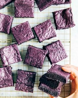 a photo of hands picking up a stack of ube brownies from a wire rack