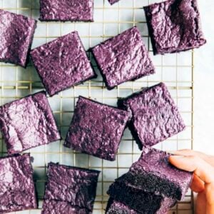 a photo of hands picking up a stack of ube brownies from a wire rack