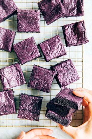 a photo of hands picking up a stack of ube brownies from a wire rack