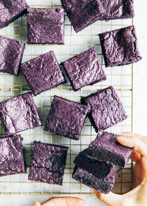 a photo of hands picking up a stack of ube brownies from a wire rack