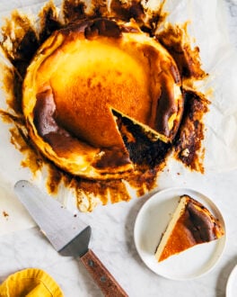 A picture of an unwrapped burnt basque cheesecake with a slice removed next to a cake server.
