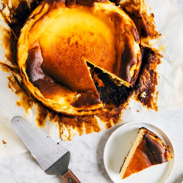 A picture of an unwrapped burnt basque cheesecake with a slice removed next to a cake server.