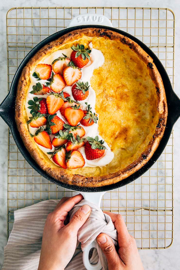 A photo of hands setting down a Dutch baby pancake on a wire rack.