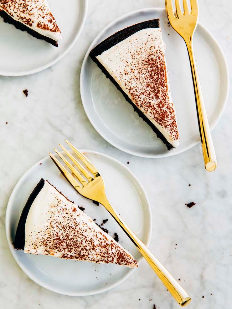 A close up photo of chocolate cake slices on a white plate with gold forks. 