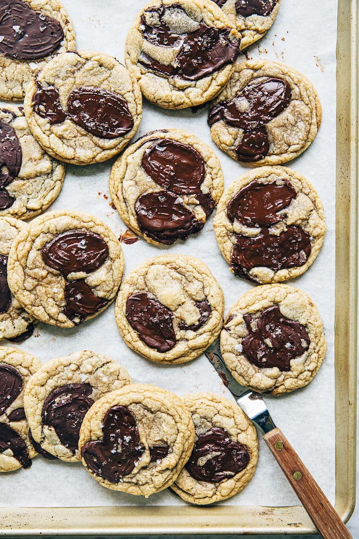 A picture of chocolate chip cookies on a gold sheet pan with an offset spatula.
