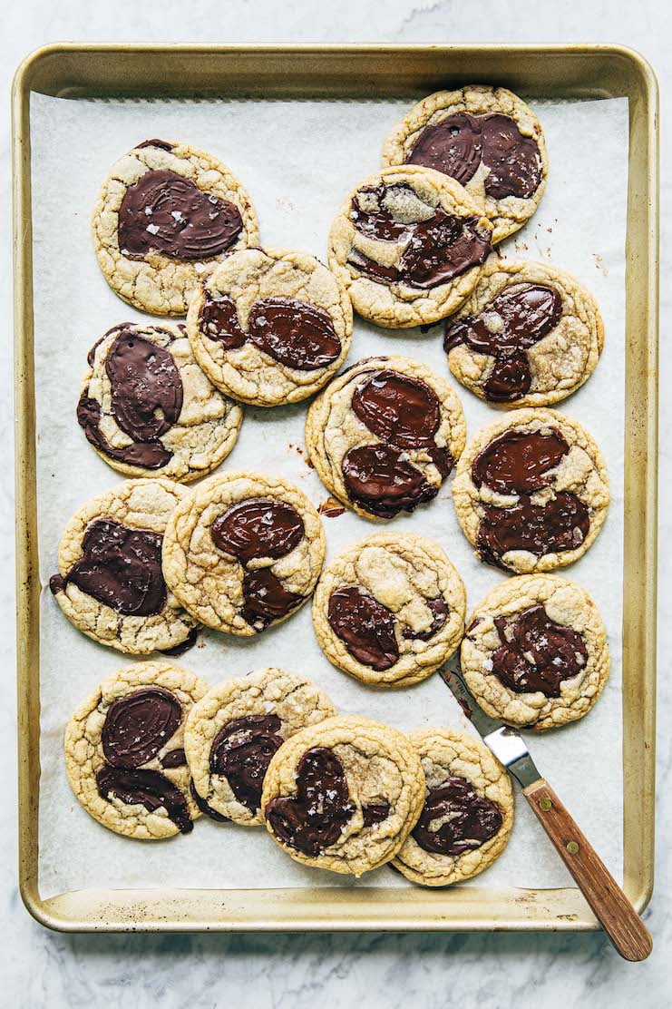 A photo of chocolate chip cookies on a gold sheet pan with an offset spatula.