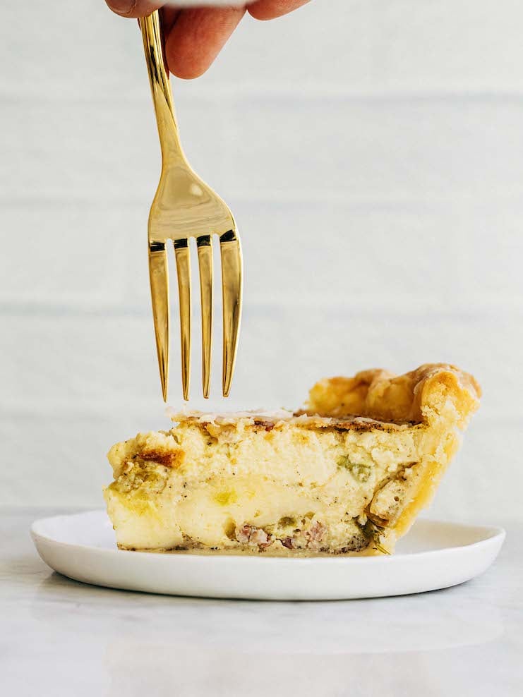 A photo of a fork piercing a slice of quiche.
