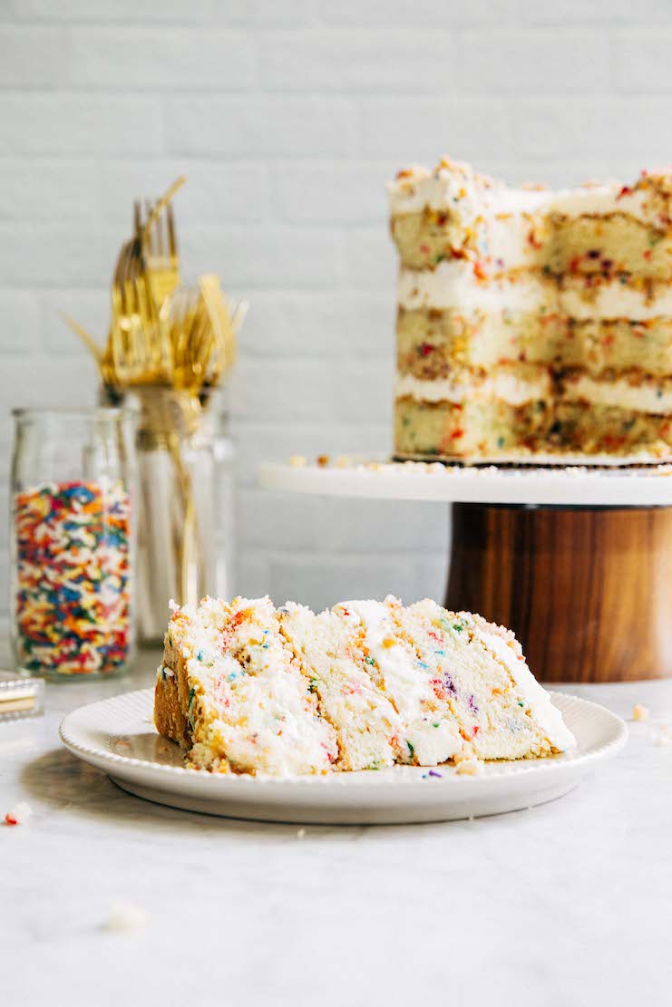 photo of sliced birthday cake on white plate with larger cake in background