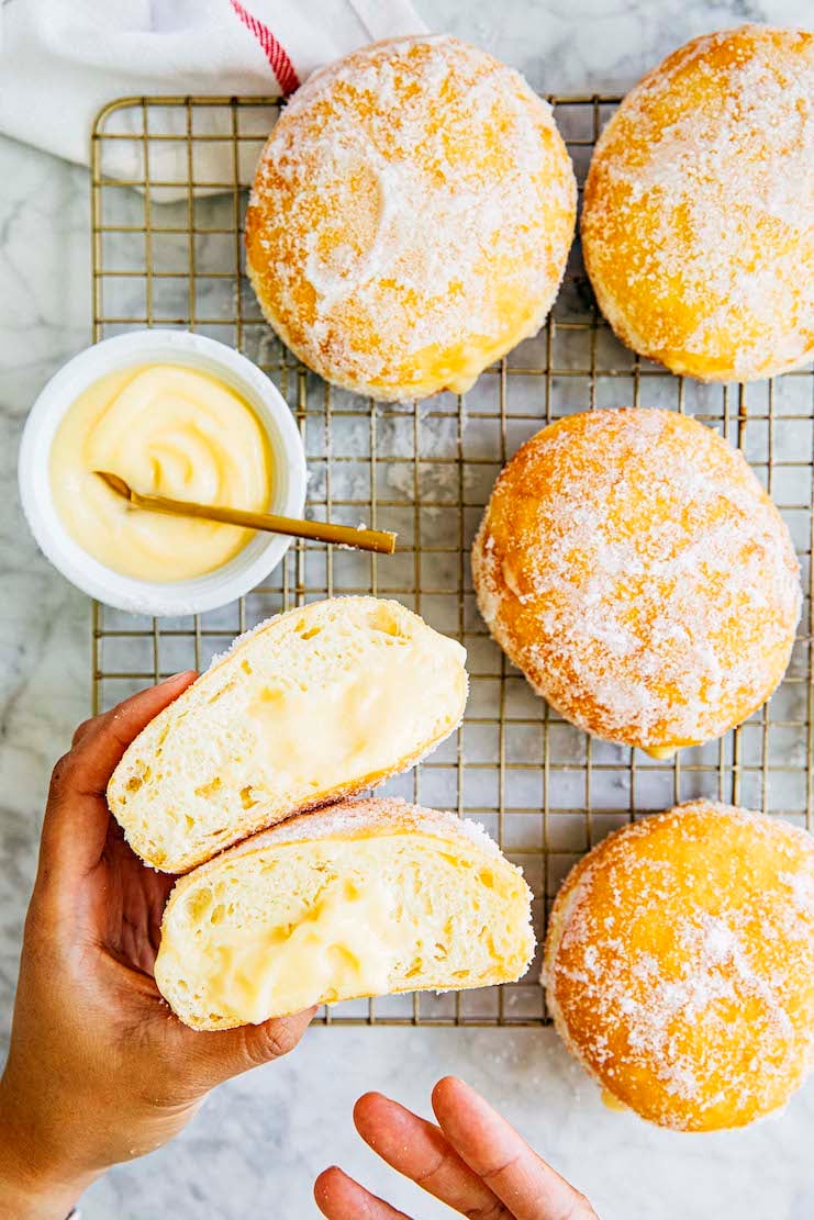 photo of hands holding a sliced malasada filled passion fruit pastry cream