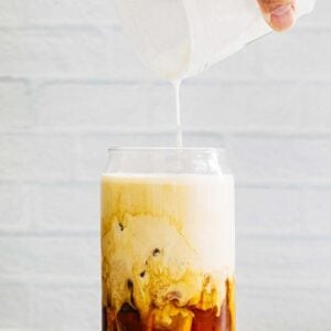 photo of hand pouring a jar of vanilla sweet cream cold foam over a glass of iced coffee