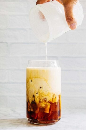 photo of hand pouring a jar of vanilla sweet cream cold foam over a glass of iced coffee