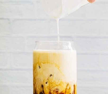 photo of hand pouring a jar of vanilla sweet cream cold foam over a glass of iced coffee