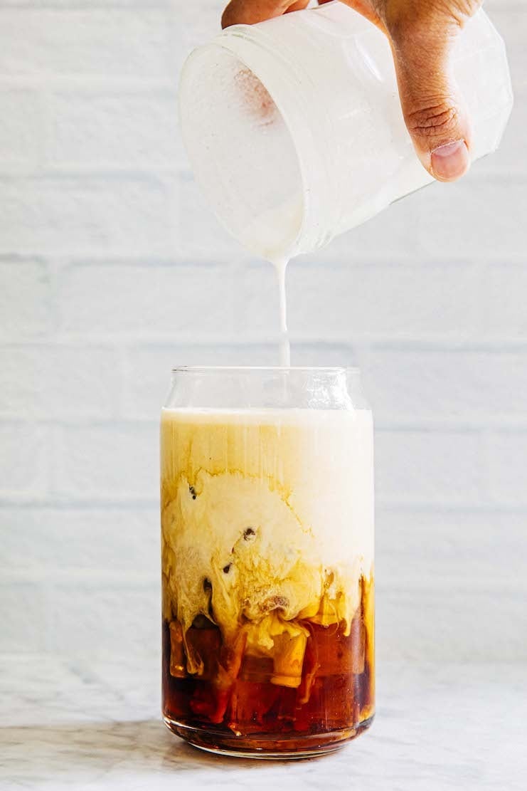 תמונה של יד מוזגת צנצנת של קצף קר עם שמנת מתוקה וניל על כוס קפה קר