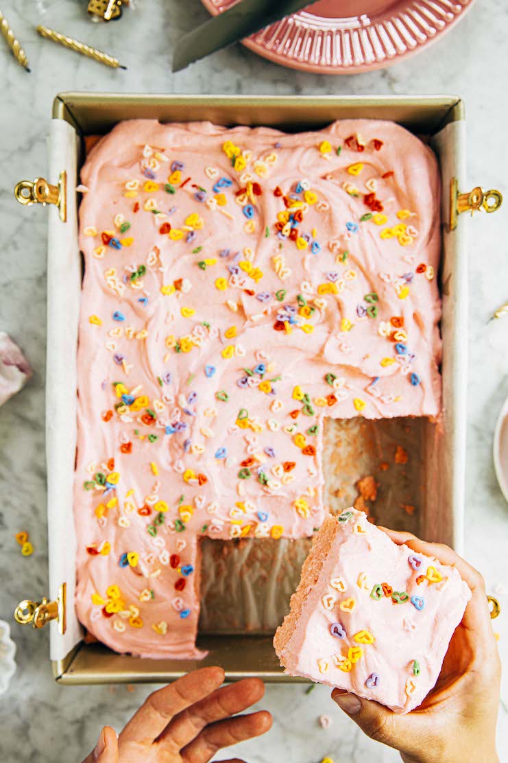 photo of pink sheet cake with hand holding up a slice of cake
