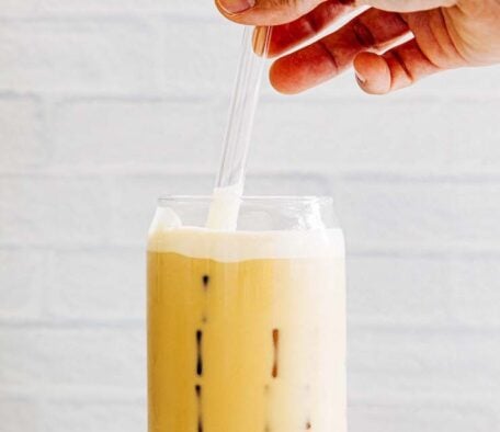 photo of hand stirring vanilla sweet cream cold foam into coffee drink