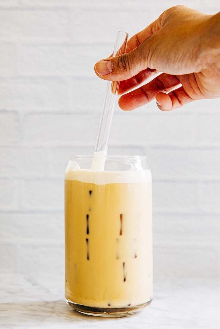 photo of hand stirring vanilla sweet cream cold foam into coffee drink