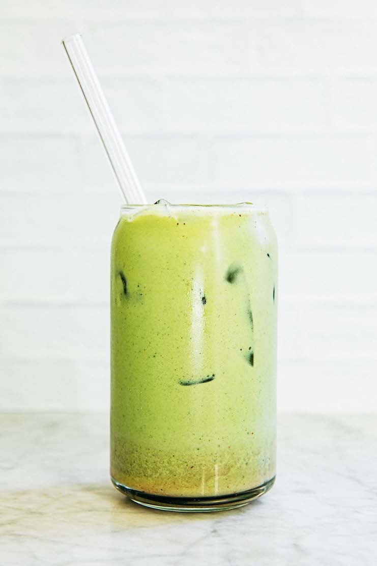 photo of matcha latte after being stirred in a clear glass against white background