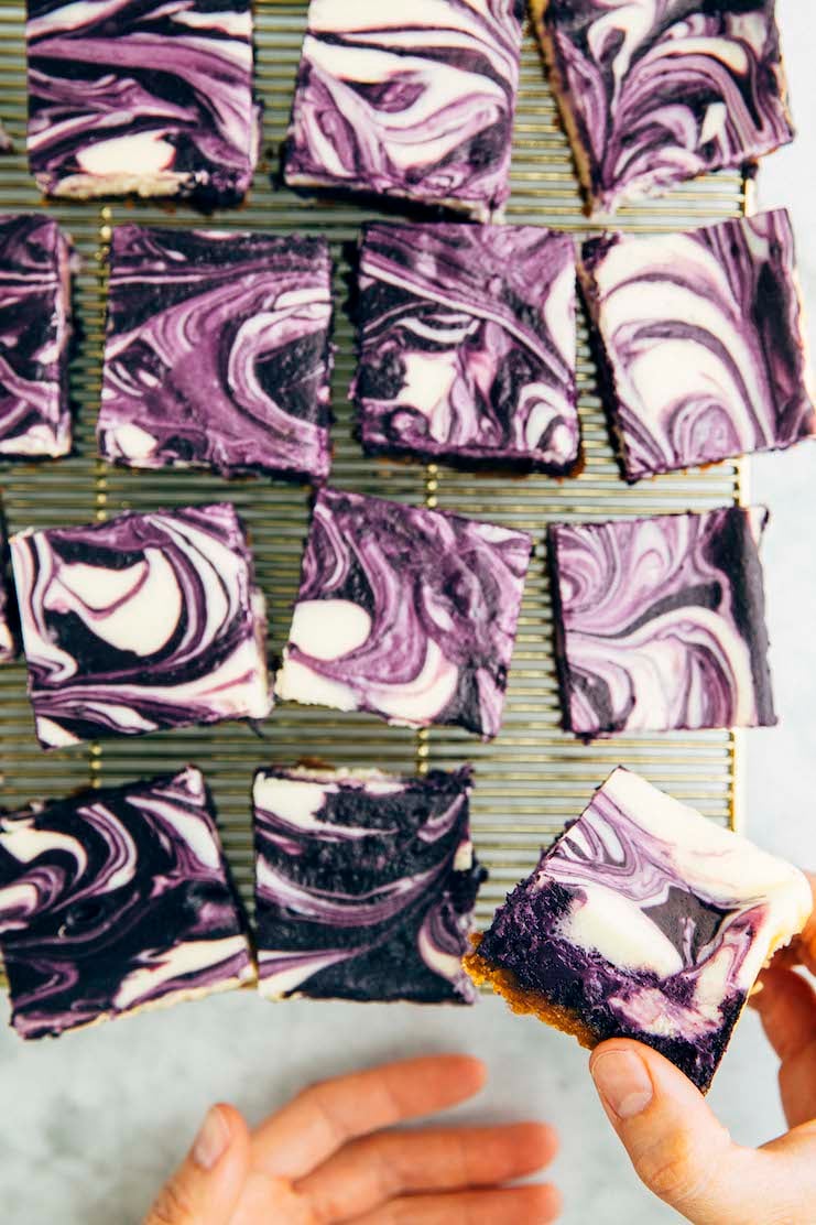 photo of hand reaching for an ube cheesecake bar showing off creamy crumb