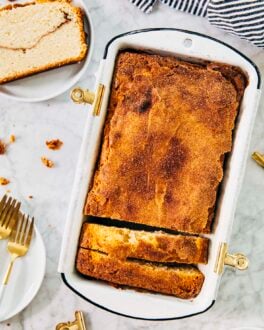 photo of snickerdoodle bread in loaf pan with a slice of the bread on a small white plate next to it