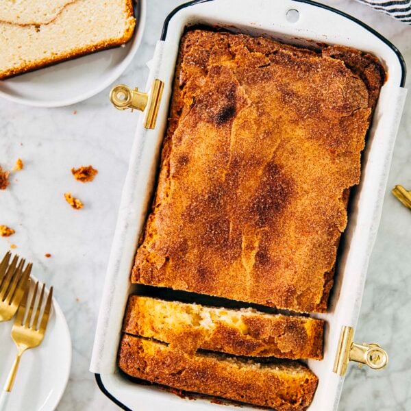 photo of snickerdoodle bread in loaf pan with a slice of the bread on a small white plate next to it