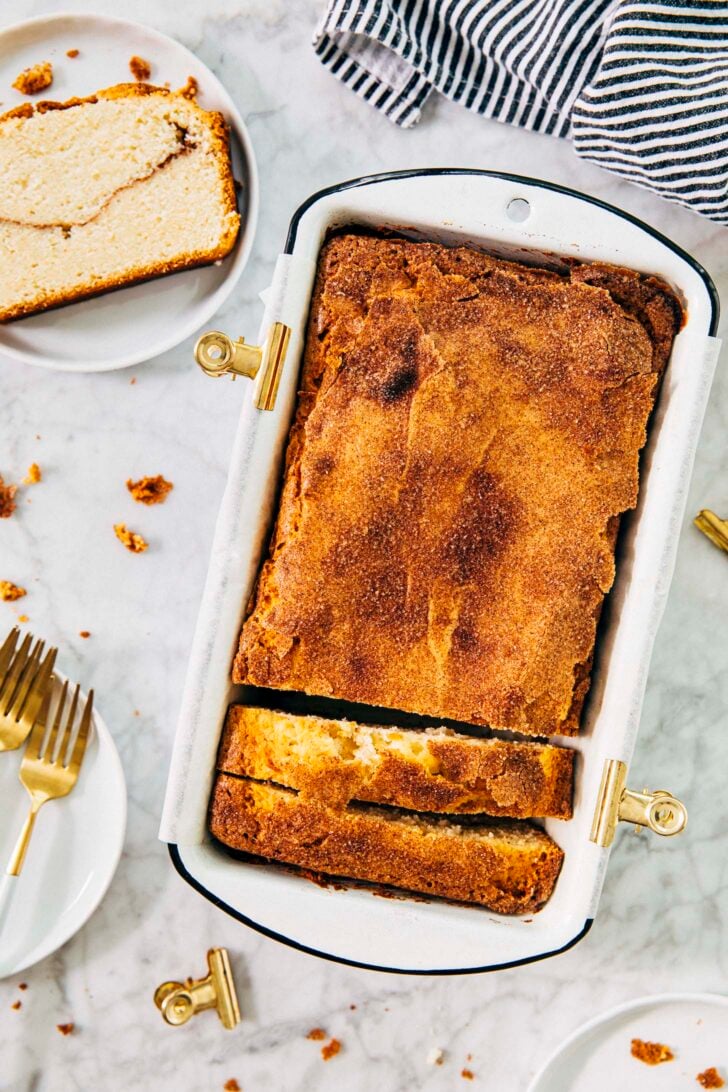 photo of snickerdoodle bread in loaf pan with a slice of the bread on a small white plate next to it