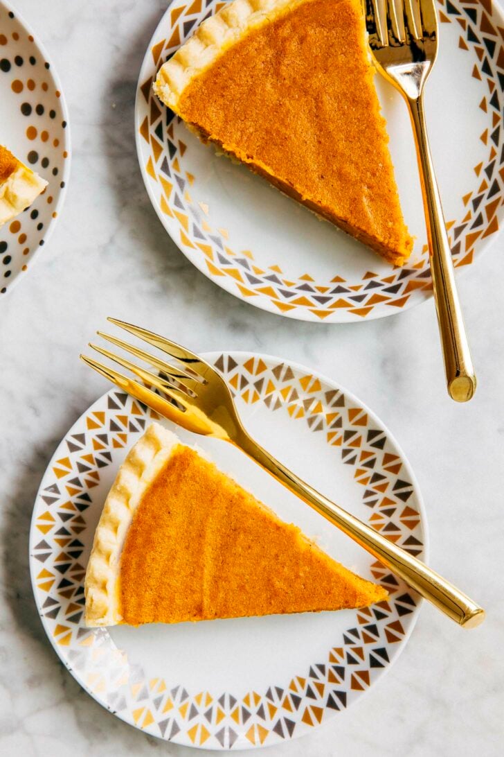 close up photo of two cream cheese pumpkin pie on white plates with gold decor and a gold forks