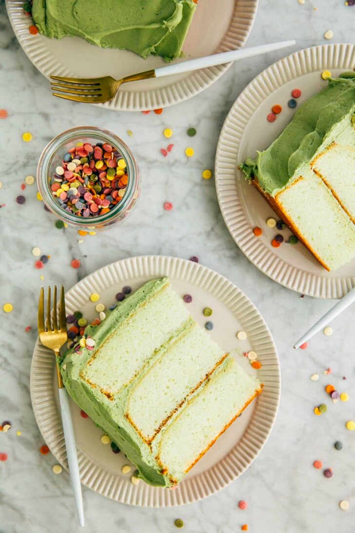 photo of pistachio pudding layer cake slices on white plates on a marble tabletop