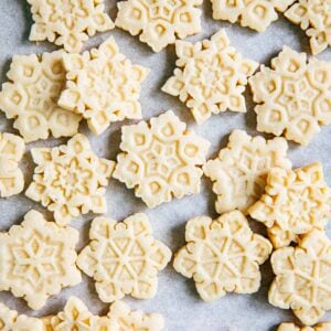 close up photo of cut out sugar cookies in the shape of snowflakes on parchment paper