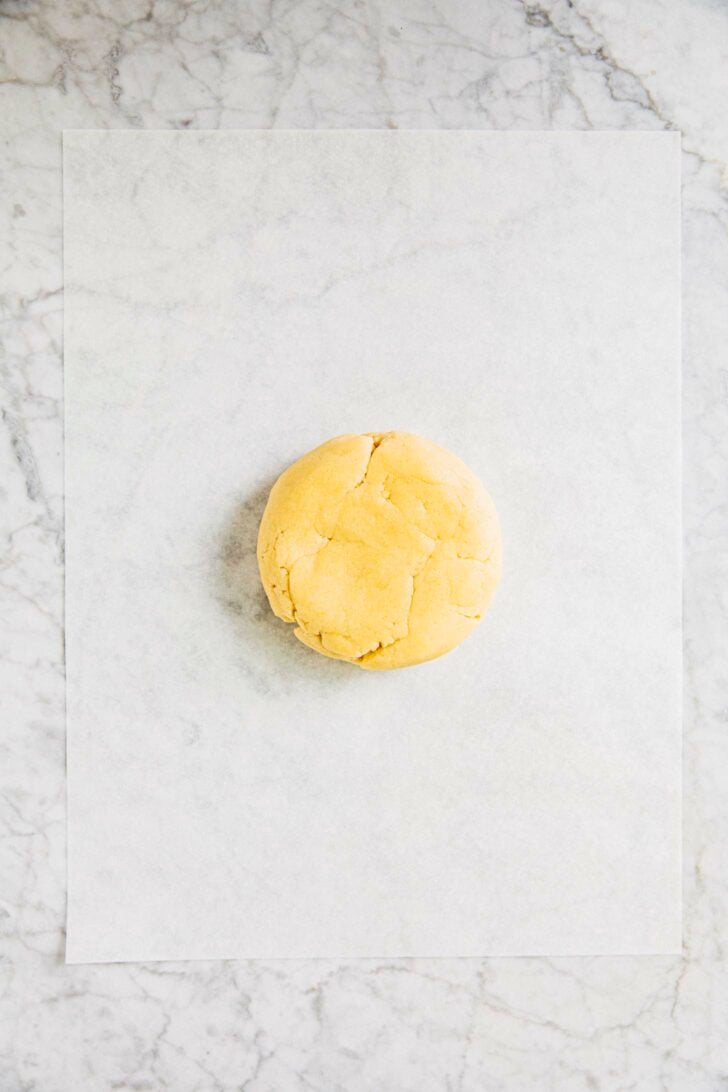 photo of cut out sugar cookie dough on a piece of parchment paper on a marble tabletop
