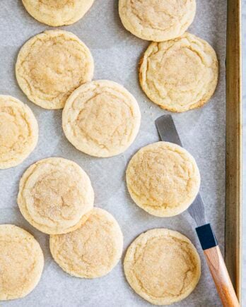 photo of drop sugar cookies on a gold sheet pan with an offset spatula