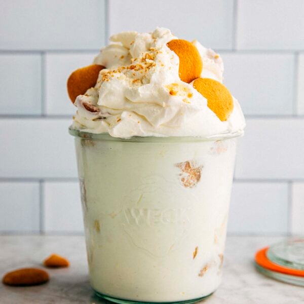 photo of a heaping small batch banana pudding in a pint jar with cookies scattered around the jar