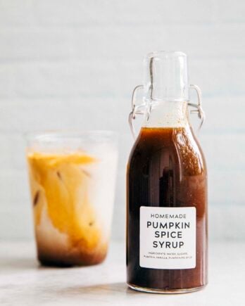 photo of homemade pumpkin spice syrup in a clear bottle next to a glass of iced coffee