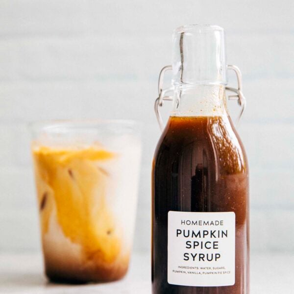 photo of homemade pumpkin spice syrup in a clear bottle next to a glass of iced coffee