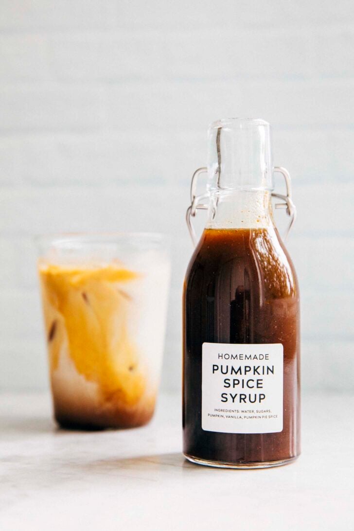 photo of homemade pumpkin spice syrup in a clear bottle next to a glass of iced coffee