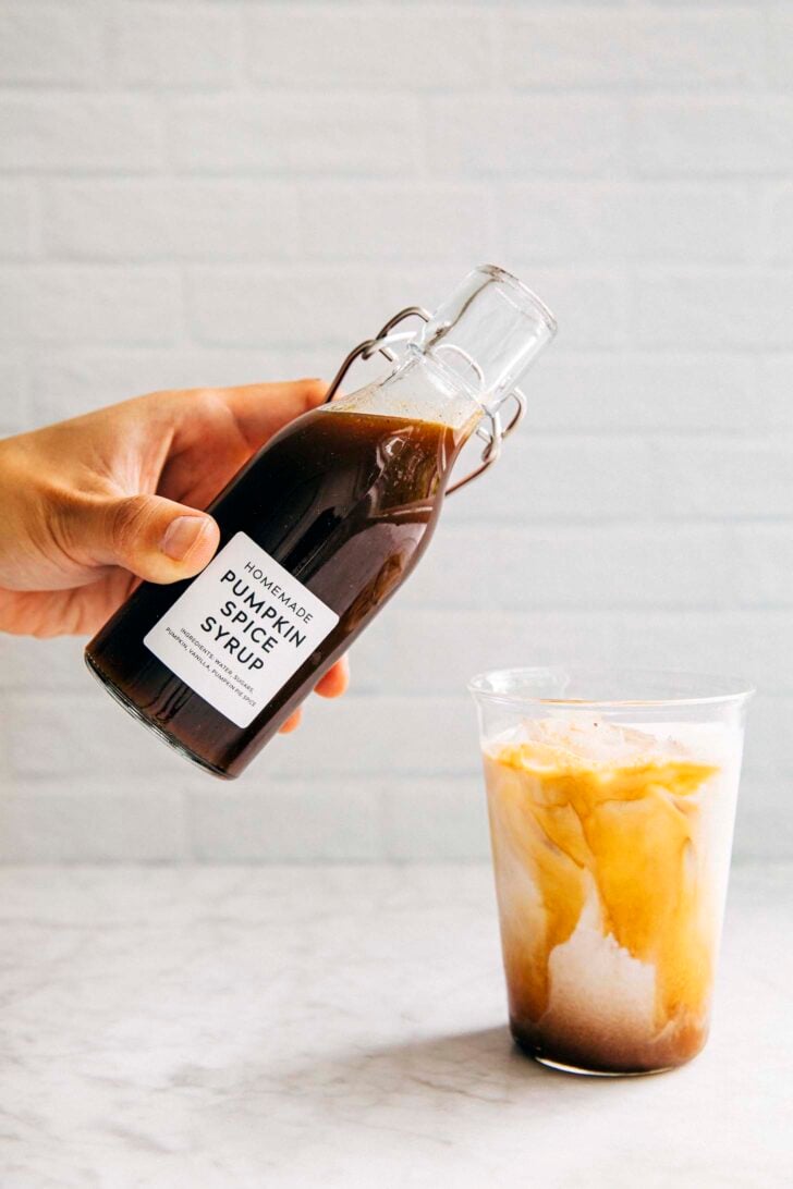 photo of michelle from hummingbird high pouring homemade pumpkin spice syrup into a glass of iced coffee