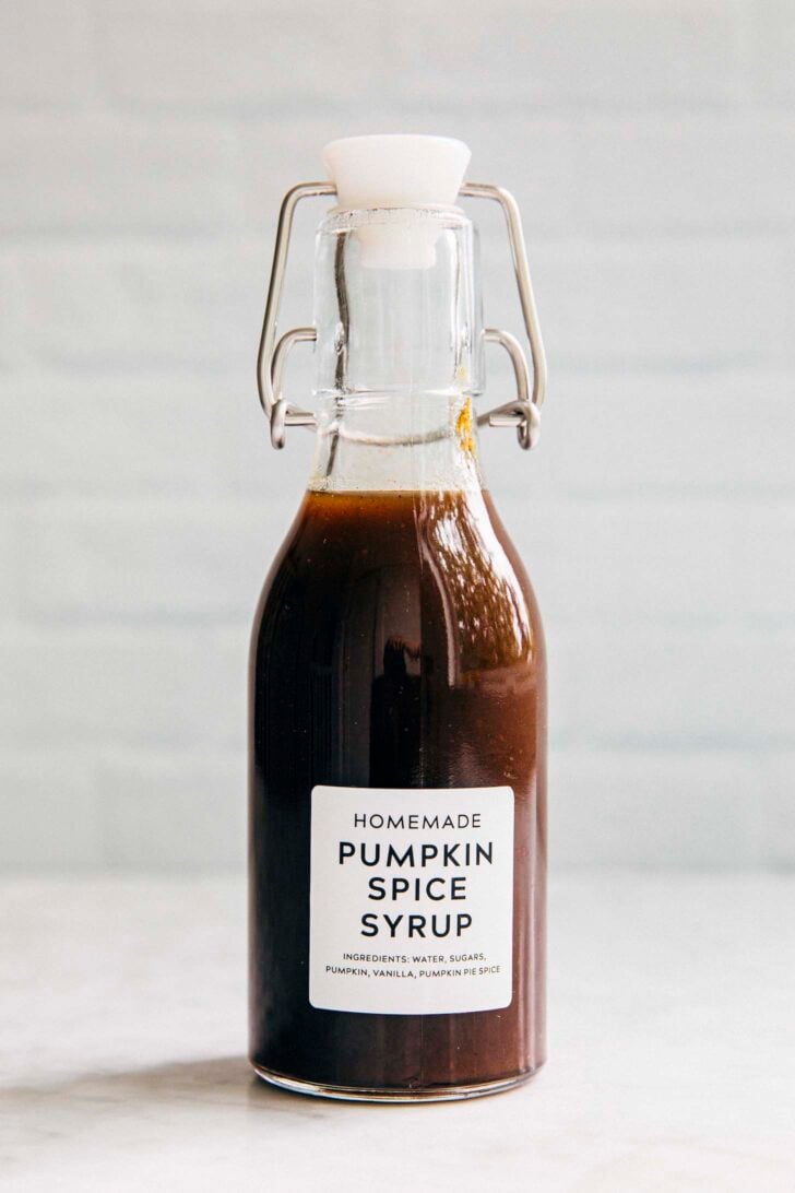 photo of homemade pumpkin spice syrup in a clear bottle against a white brick backdrop