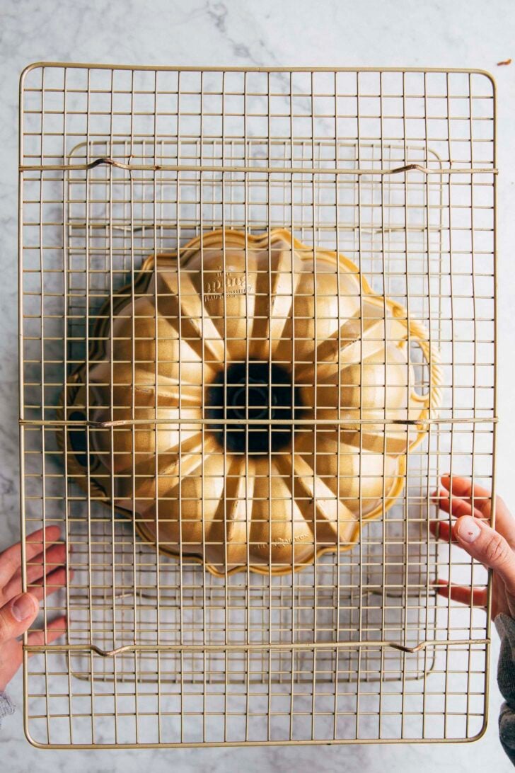 photo of michelle flipping the bundt cake pan upside down between the two wire racks to turn out the bundt cake